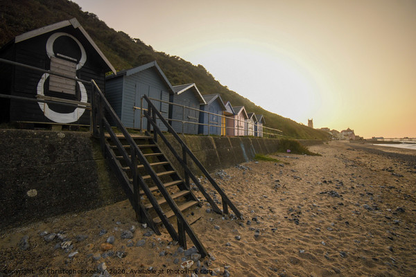 Sunset over Cromer beach huts Picture Board by Christopher Keeley