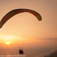Buy canvas prints of Tandem paragliding over sea and beach while golden by Hanif Setiawan