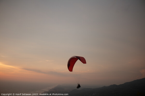 Tandem paragliding over sea and beach at sunset Picture Board by Hanif Setiawan