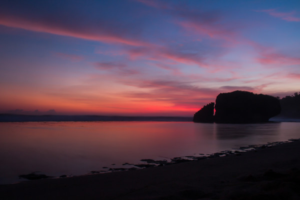 Silhouetted reflecting rock at sunset on sandbeach Picture Board by Hanif Setiawan