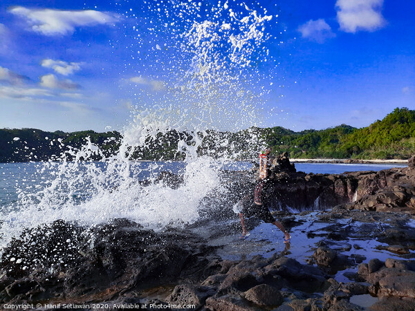 A big wave hits a man on a rock plateau Picture Board by Hanif Setiawan