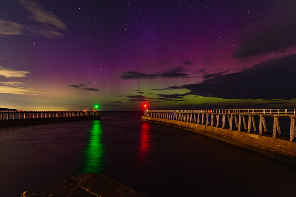 Northern Lights over the piers in Whitby Picture Board by Kevin Winter