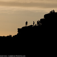 Buy canvas prints of Silhouette of lots of people watching a climber at the summit of stanage edge. Climber wears a harness with tools like nuts, ropes and carabiners. by Rhys Leonard
