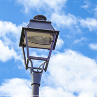 Buy canvas prints of A low angle shot of an old metal street lamp against blue cloudy sky by Ingo Menhard
