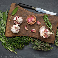 Buy canvas prints of Still life, Garlic on a chopping board with herbs by Thomas Klee