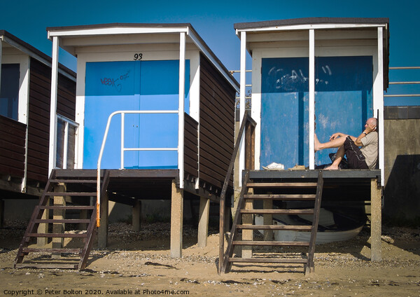 Beach huts at Thorpe Bay, Essex, with a person sitting on the floor talking on the phone. Picture Board by Peter Bolton