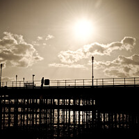 Buy canvas prints of Sepia image of part of Southend Pier shot against the sun, with silhouette of structure and a man on the walkway. Southrnd on Sea, Essex. by Peter Bolton
