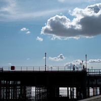 Buy canvas prints of Part of the walkway in silhouette at Southend Pier, Essex, UK, with isolated clouds overhead. by Peter Bolton