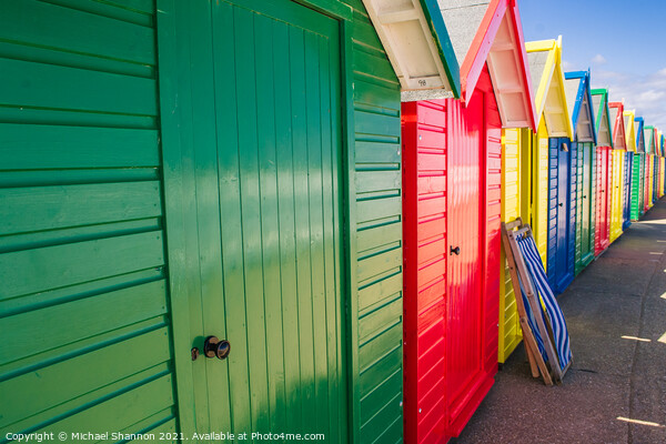 Colourful Beach Huts and a deck chair in Whitby Picture Board by Michael Shannon