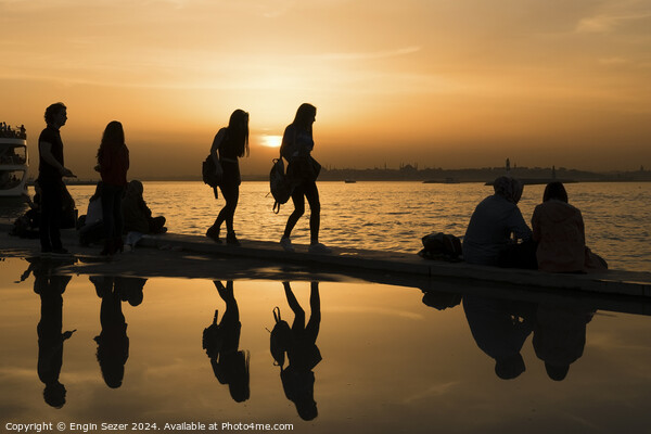 Silhouettes of some young people with beautiful reflections on the water at sunset Picture Board by Engin Sezer