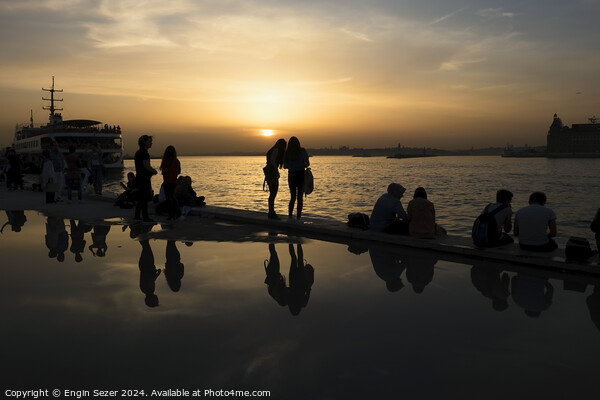 Silhouettes of some young people with beautiful reflections on the water at sunset Picture Board by Engin Sezer
