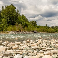 Buy canvas prints of A boulder strewn, fast flowing river, beside a forest, on a cloudy day. by SnapT Photography