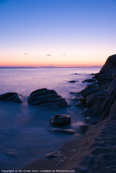 Long exposure of sea around rocks on beach Picture Board by Nic Croad