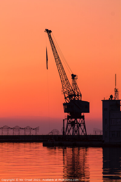 Port crane at sunset Picture Board by Nic Croad