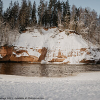 Buy canvas prints of rock cliff and cave by the river Gauja in the Gauja National Park in Latvia in winter with beautiful sun through the forest by Emils Vanags