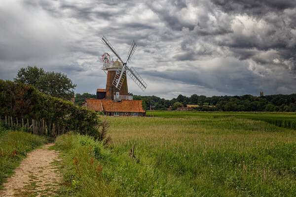 Outdoor field with a windmill under dramatic stormy sky Picture Board by John Gilham