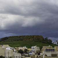 Buy canvas prints of Storm over the hill with buildings, Gozo Island. by Maggie Bajada