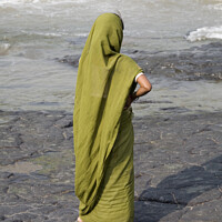 Buy canvas prints of Indian lady dressed in green stands on a rock looking at the ocean - Mumbai  by Gordon Dixon