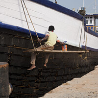 Buy canvas prints of A ship repairer paints an old wooden ship in Mangalore, India by Gordon Dixon