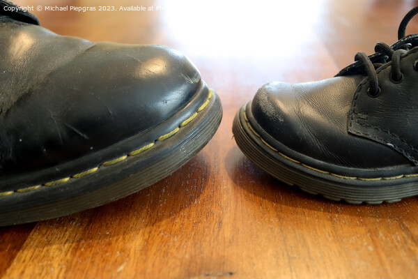 Big and small old black leather shoe on a wooden floor Picture Board by Michael Piepgras