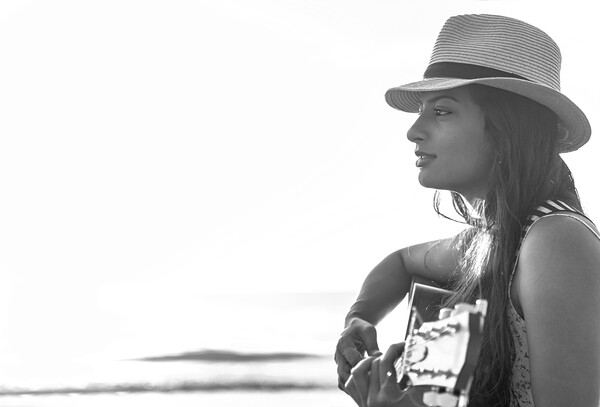 Indian woman wearing hat playing guitar on beach Picture Board by Spotmatik 