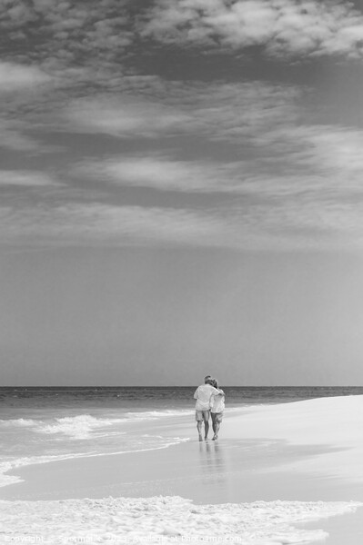Retired couple walking by ocean in loving embrace Picture Board by Spotmatik 