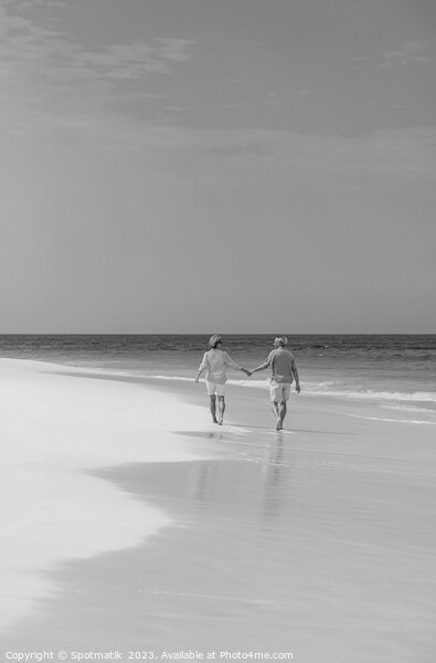 Retired couple holding hands enjoying walk on beach Picture Board by Spotmatik 