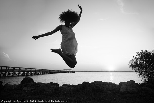 African American woman jumping by ocean at sunset Picture Board by Spotmatik 