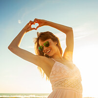 Buy canvas prints of Bohemian girl showing heart sign dancing on beach by Spotmatik 