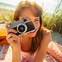Buy canvas prints of Smiling Caucasian girl with camera photographing beach vacation by Spotmatik 