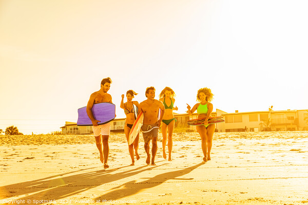 Friends in swimwear running carrying bodyboards on beach Picture Board by Spotmatik 