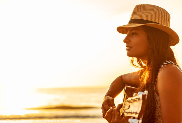 Indian woman wearing hat playing guitar on beach Picture Board by Spotmatik 