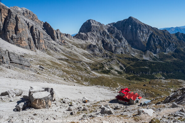 Tourist with hiking backpacks in mountain hike on summer day. Man traveler hiking in beautiful mountain landscape. Climber and alpine hut Silvio Agostini in Dolomites Alps, Italy. Picture Board by Lubos Chlubny