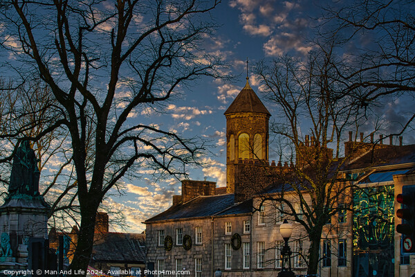 Historic stone building with a clock tower at dusk, silhouetted trees, and a vibrant sky in Lancaster. Picture Board by Man And Life