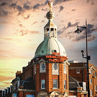 Buy canvas prints of Dramatic sky over Wimbledon Theatre with golden sunset light illuminating the building's facade and dome. by Man And Life