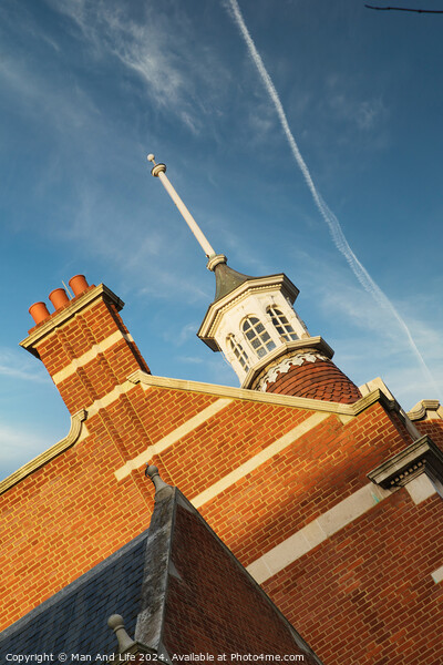 Historic brick building with a distinctive cupola against a blue sky with contrails. Picture Board by Man And Life
