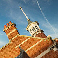 Buy canvas prints of Historic brick building with a distinctive cupola against a blue sky with contrails. by Man And Life