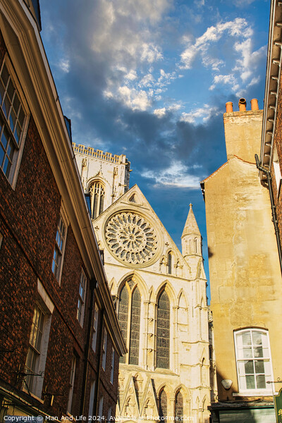 Historic cathedral facade with rose window, framed by old buildings against a blue sky with clouds in York, UK. Picture Board by Man And Life