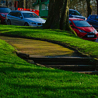 Buy canvas prints of Sunny park with green grass and a pathway leading through trees, with parked cars in the background in Harrogate, England. by Man And Life