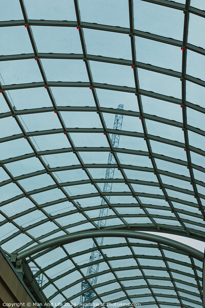 Abstract view of a glass ceiling with a metal frame, showcasing geometric patterns and a clear blue sky in the background. Picture Board by Man And Life