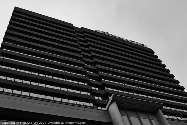 Modern black and white architectural photograph of a high-rise building with a patterned facade against a cloudy sky in Leeds, UK. Picture Board by Man And Life
