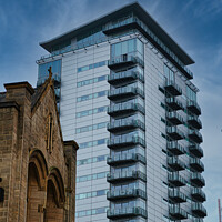 Buy canvas prints of Contrast of old and new architecture with a modern glass skyscraper towering behind a traditional stone church under a clear blue sky in Leeds, UK. by Man And Life