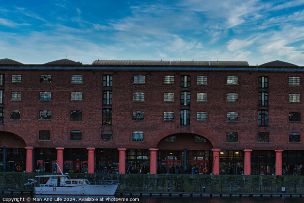 Brick warehouse with arched supports by a canal with a moored boat under a clear blue sky in Liverpool, UK. Picture Board by Man And Life
