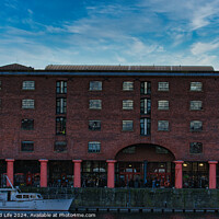 Buy canvas prints of Brick warehouse with arched supports by a canal with a moored boat under a clear blue sky in Liverpool, UK. by Man And Life