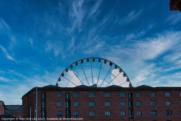 Ferris wheel silhouette against a blue sky with wispy clouds, framed by buildings in Liverpool, UK. Picture Board by Man And Life