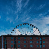Buy canvas prints of Ferris wheel silhouette against a blue sky with wispy clouds, framed by buildings in Liverpool, UK. by Man And Life