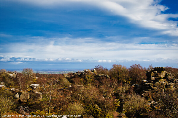 Scenic view of rocky terrain with lush greenery under a blue sky with fluffy clouds, overlooking a distant body of water at Brimham Rocks, in North Yorkshire Picture Board by Man And Life