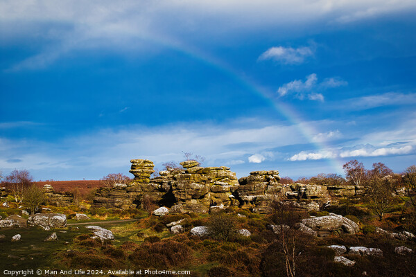 Vibrant rainbow over a rocky landscape with scattered boulders and lush greenery under a blue sky with clouds at Brimham Rocks, in North Yorkshire Picture Board by Man And Life
