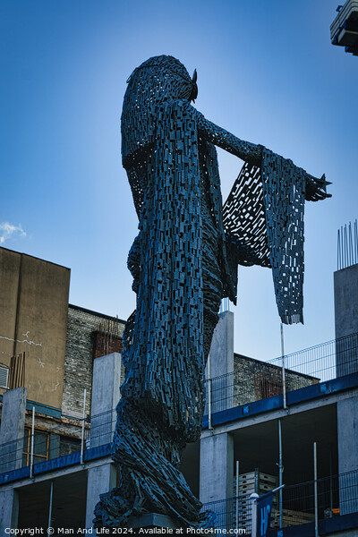 Artistic metal sculpture of a humanoid figure against a clear blue sky, with urban buildings in the background in Leeds, UK. Picture Board by Man And Life