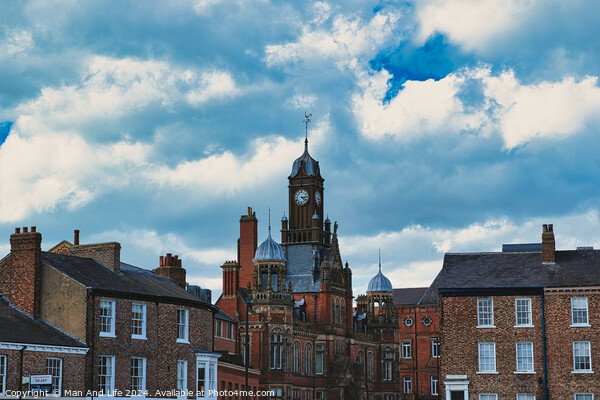 Dramatic clouds loom over a historic town center, featuring a prominent clock tower and classic brick buildings, capturing a quintessential British townscape in York, North Yorkshire, England. Picture Board by Man And Life